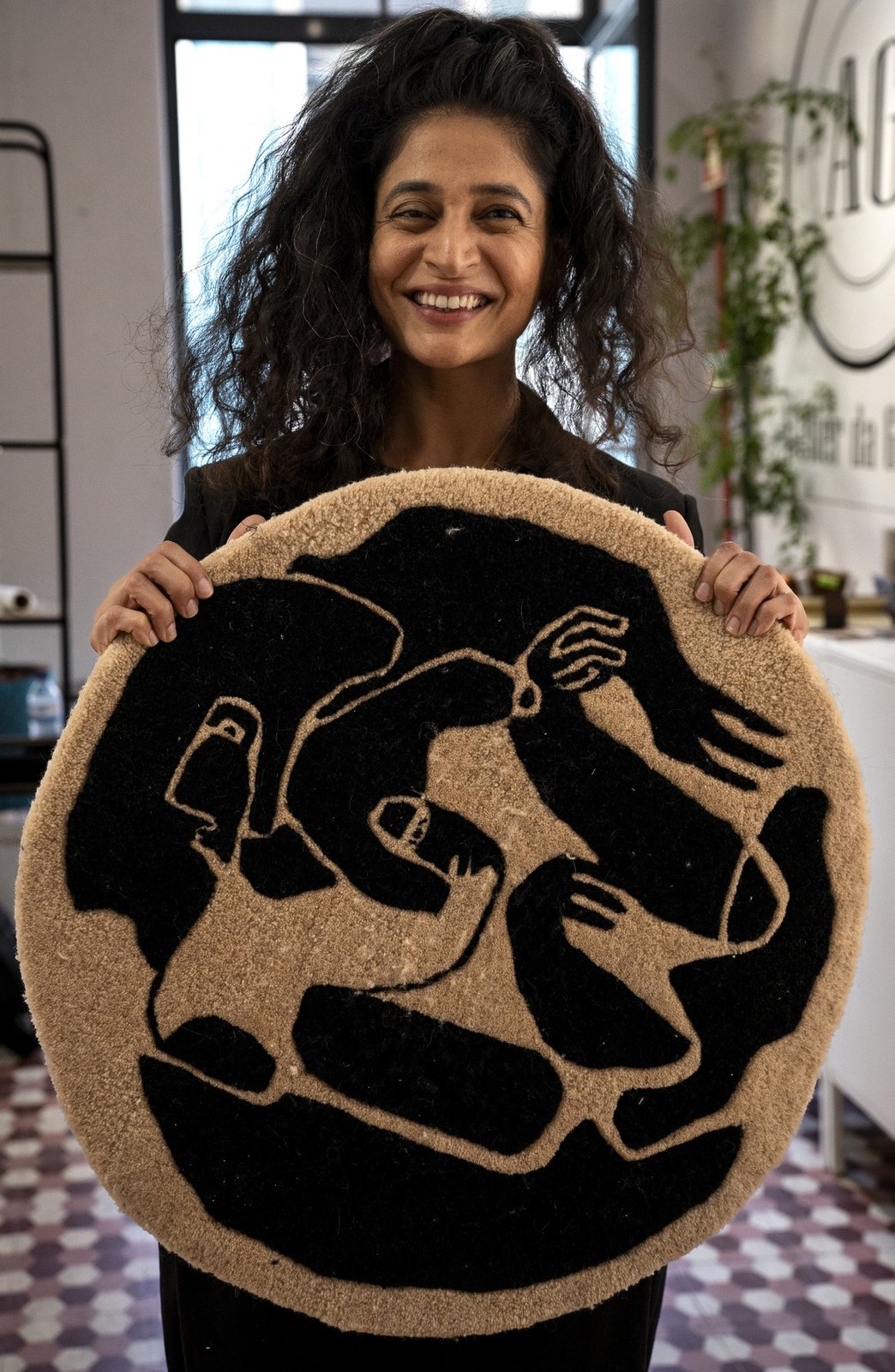 Holding a round tufted rug of two entwined figures.