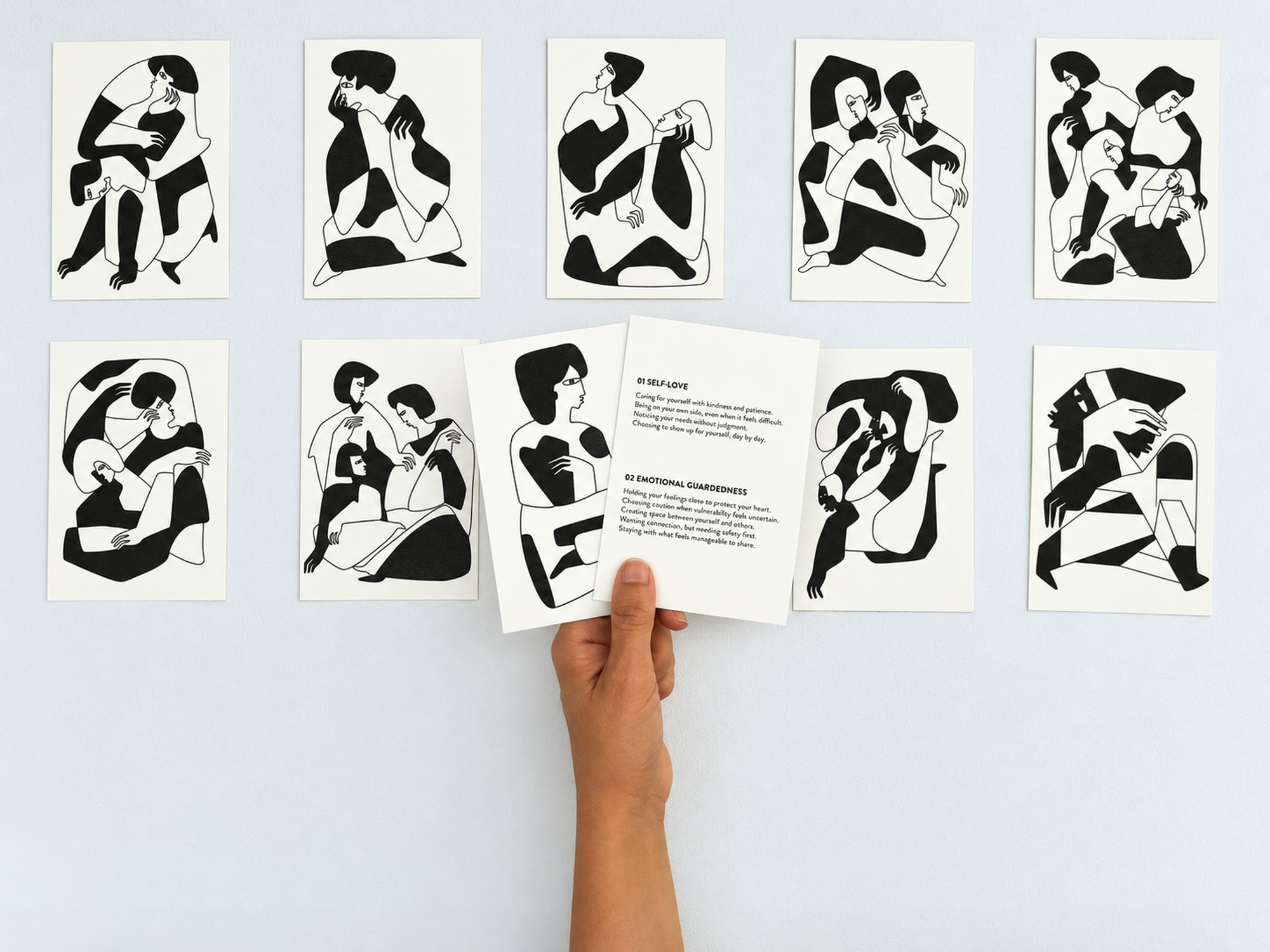 The ten printed emotion cards laid out in two rows, with a hand holding the self-love card, front and back.
