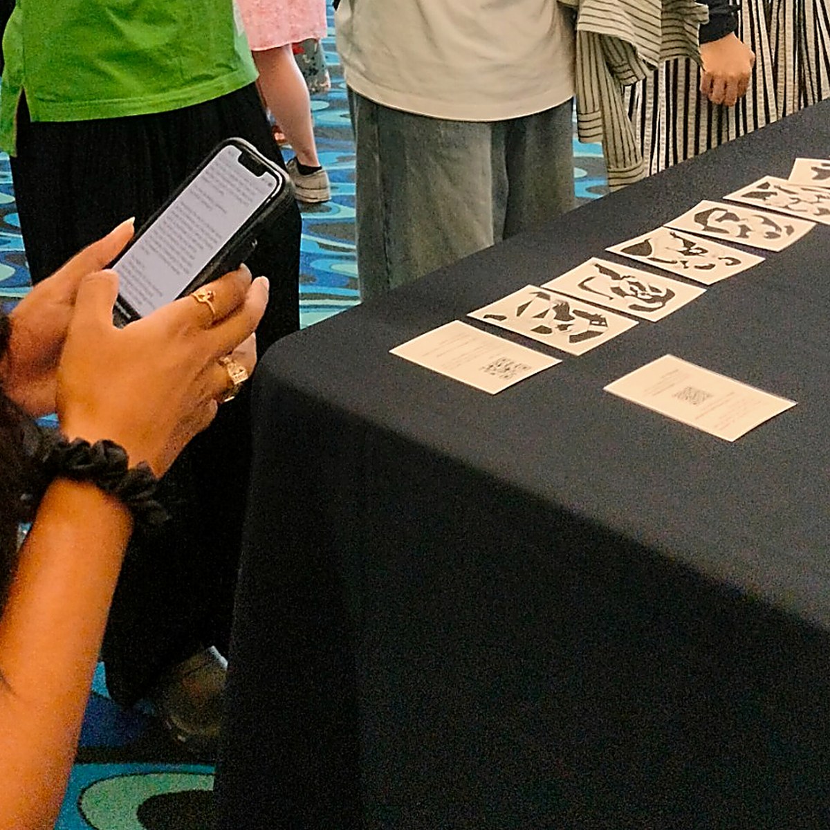 Over a visitor’s shoulder: hands holding a phone with the reflection page open, beside a long table of emotion cards and QR instruction cards.