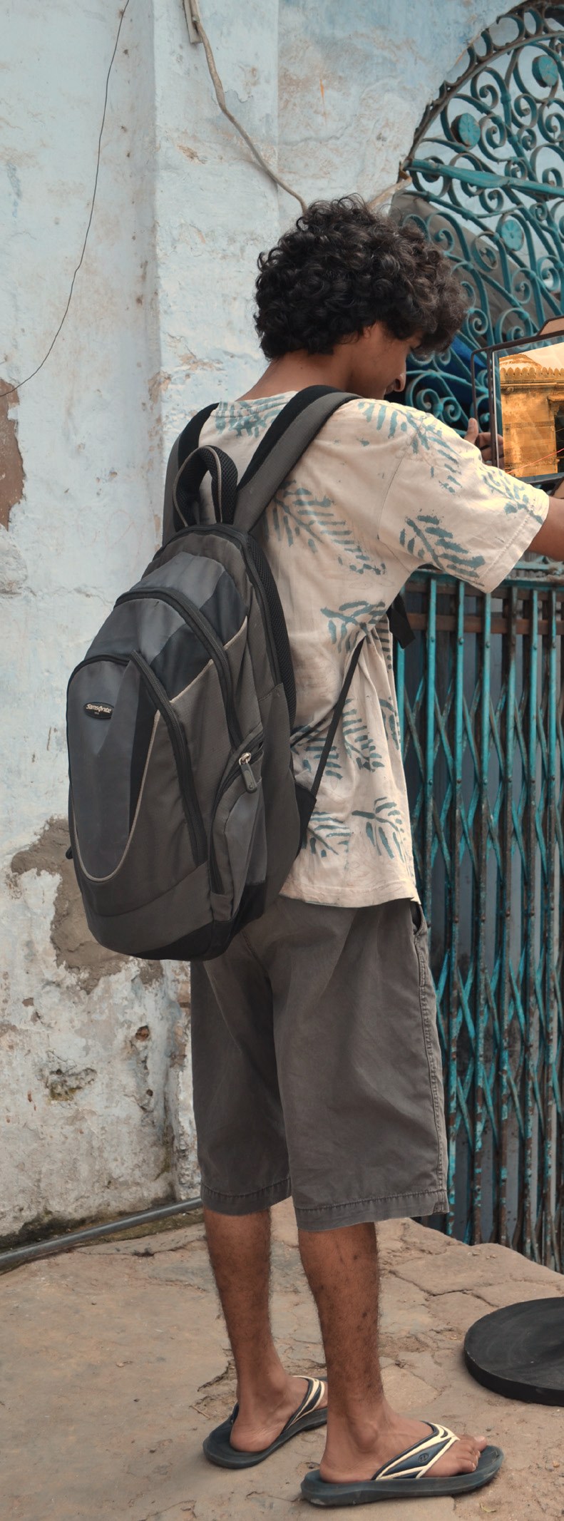 A visitor with a backpack, seen from behind, using the frame beside a blue doorway.