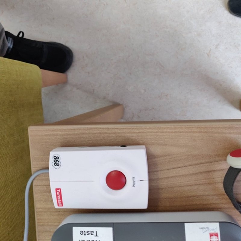 A home emergency alarm unit with a red button and a wrist button.
