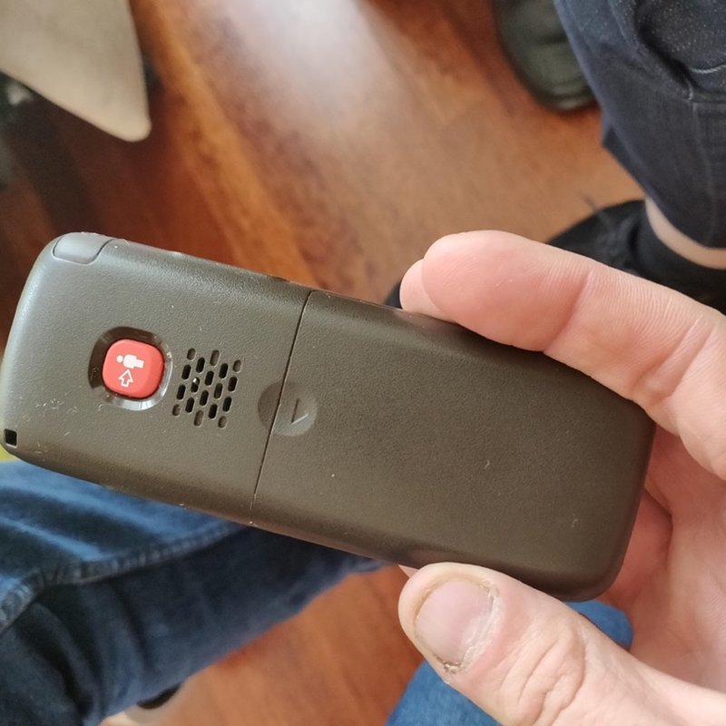 A hand holding a simple phone with a single red emergency button.