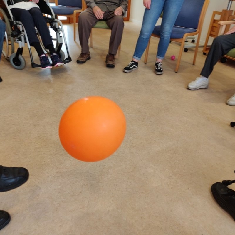 A ball on the floor in the middle of a circle of chairs, with only legs and feet visible.