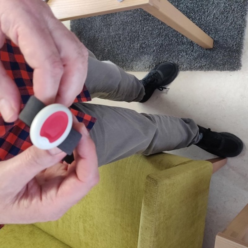 Hands holding a round wrist alarm button with a red centre.